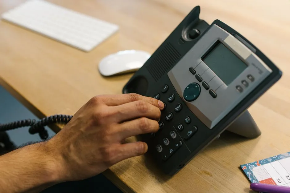 A hand dialing a desk phone for the short fit call