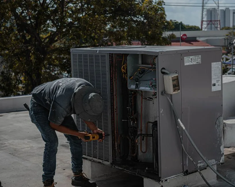 HVAC technician working on a condenser unit beside a house